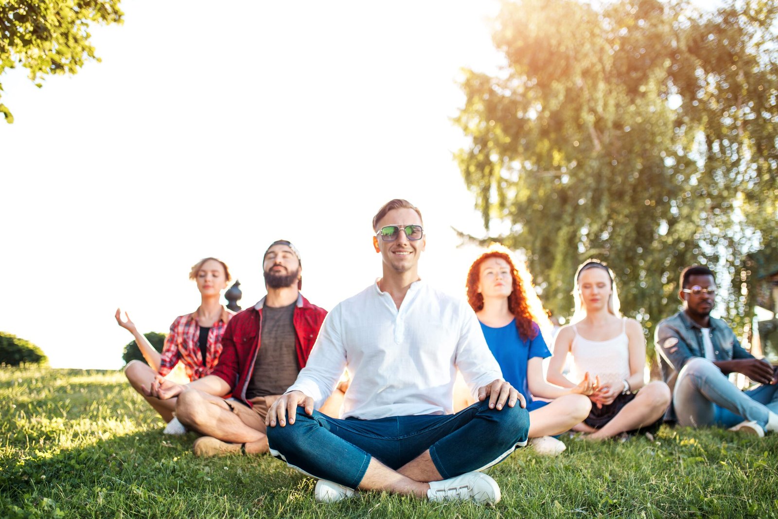 Group of adult mix-race friends meditating while practice yoga outside in park.