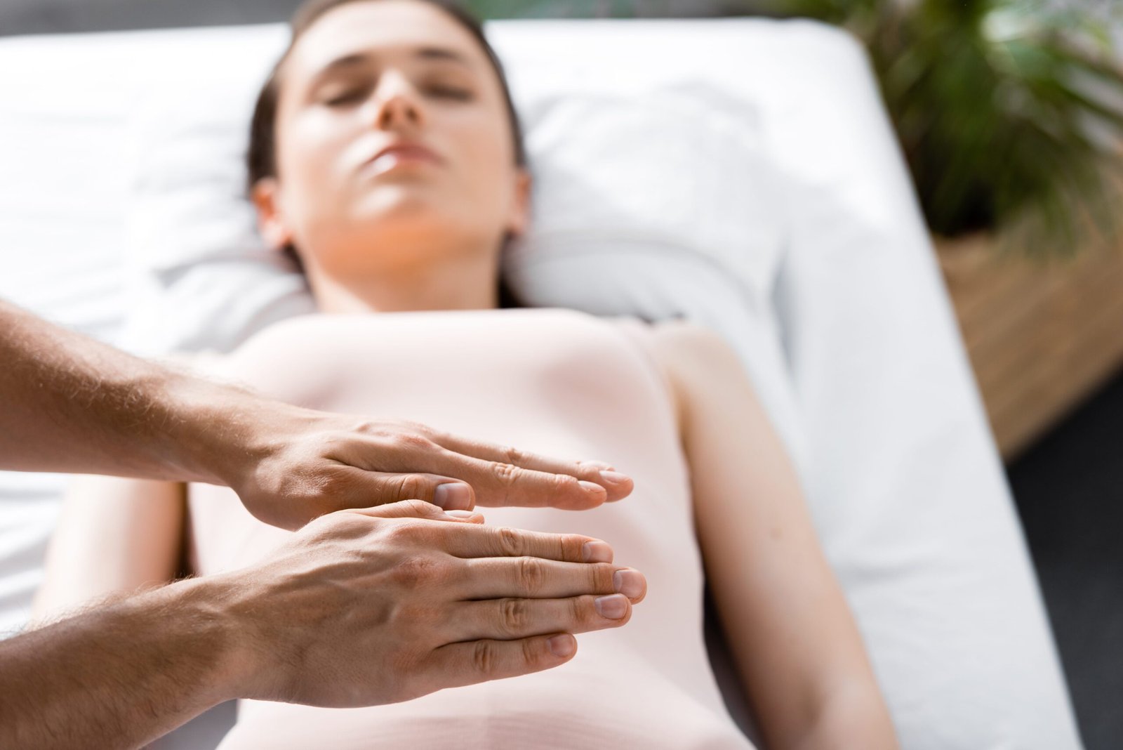 cropped view of healer standing near woman lying with closed eyes on massage table and holding hands